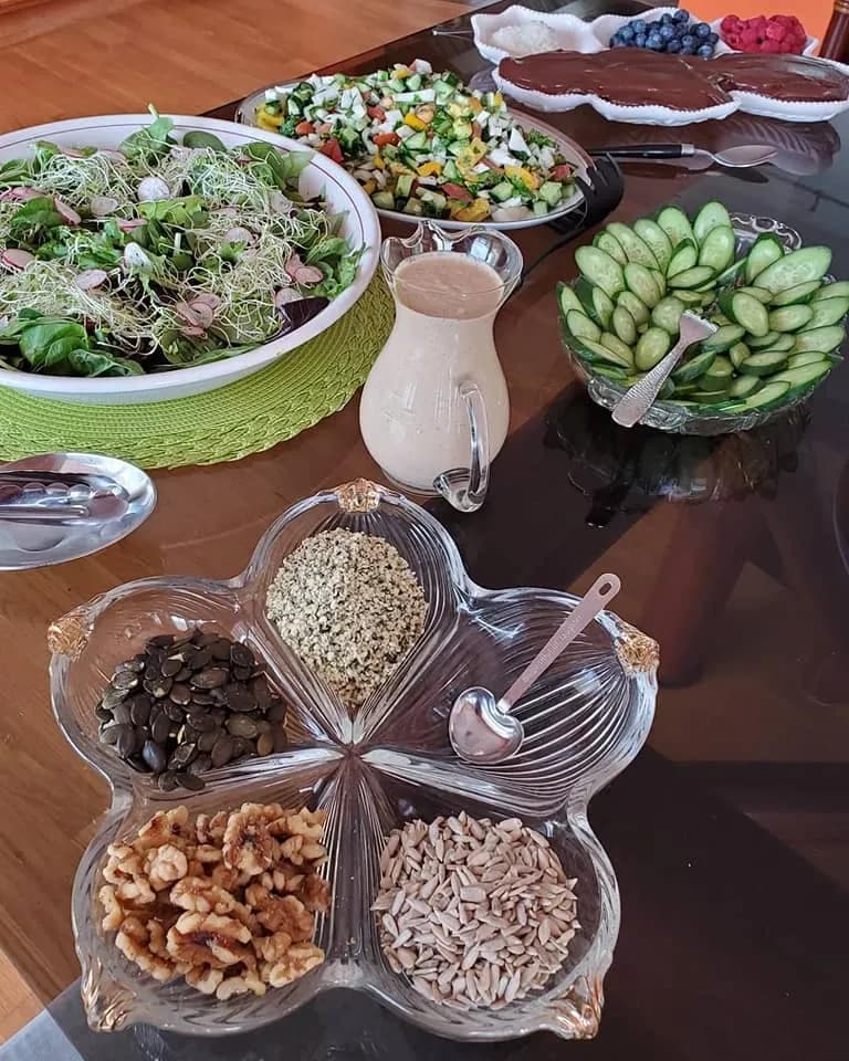 A colorful spread of salads, nuts, seeds, cucumbers, and a creamy dressing on a table.