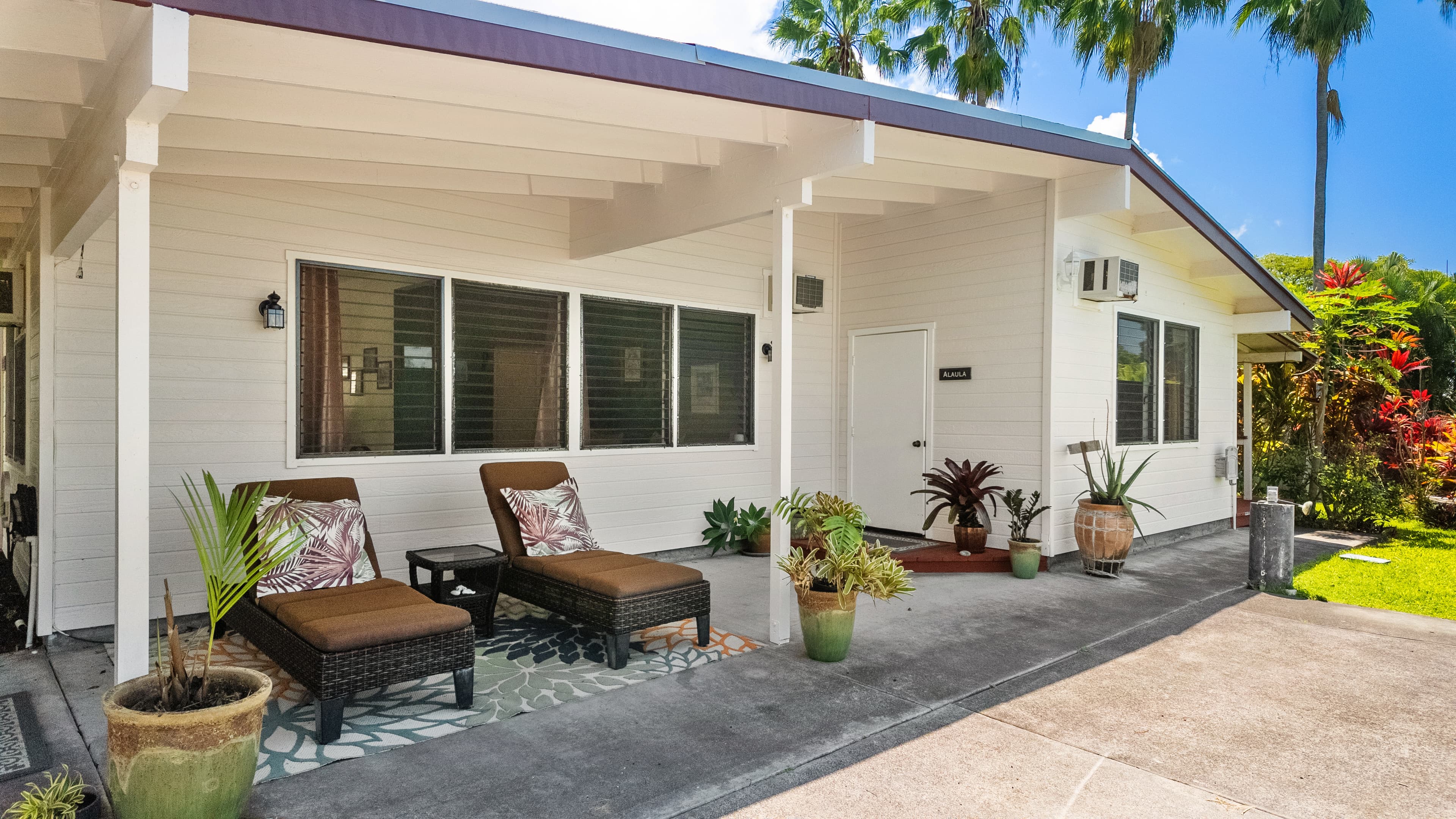 A cozy porch with two lounge chairs and potted plants in front of a white house.
