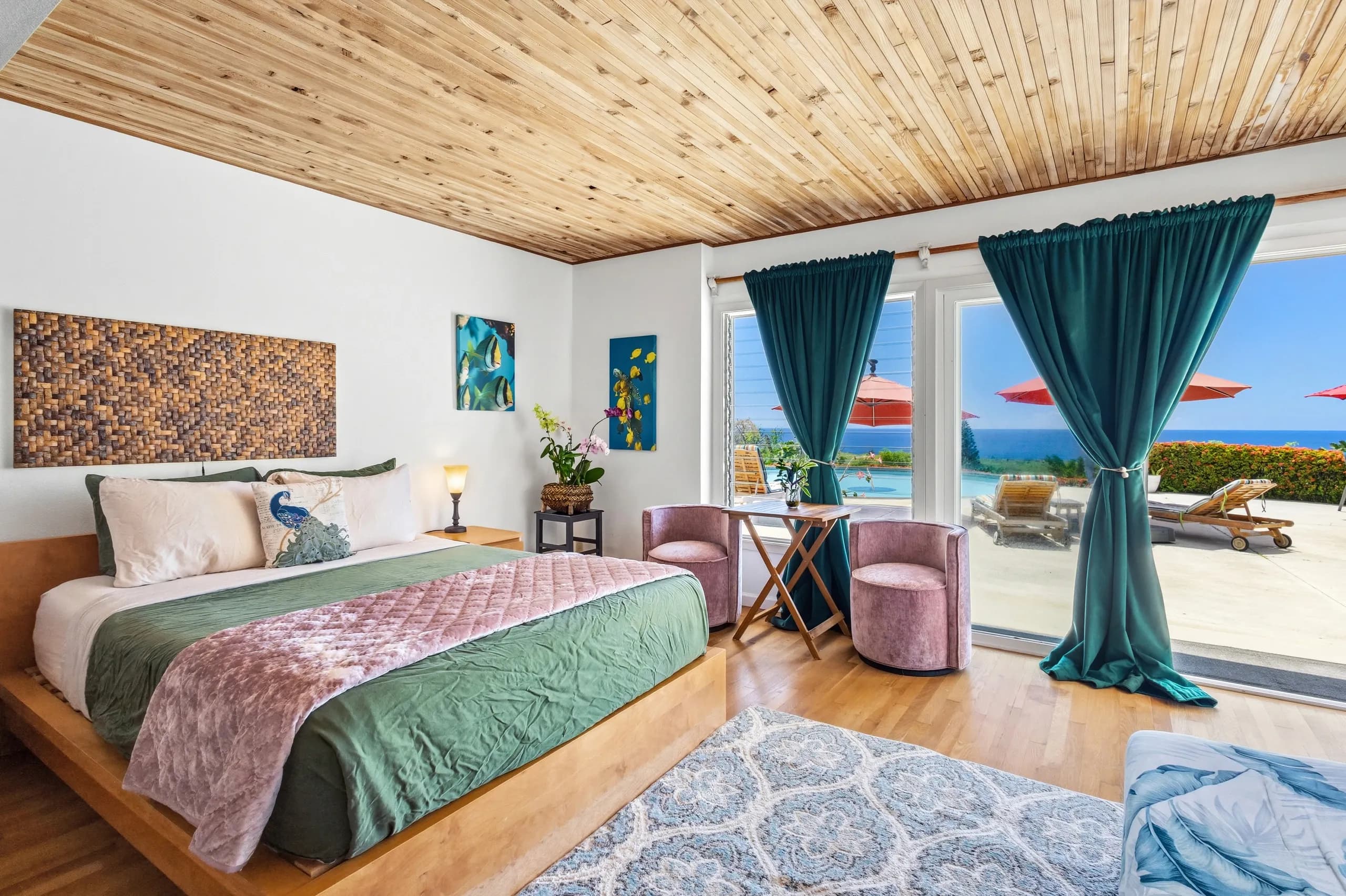 Bright, modern bedroom featuring a king-size bed, vibrant decor, and large windows overlooking a patio with umbrellas.