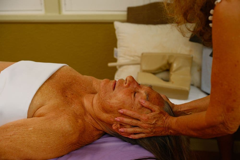 A woman receives a facial massage while lying on a massage table.