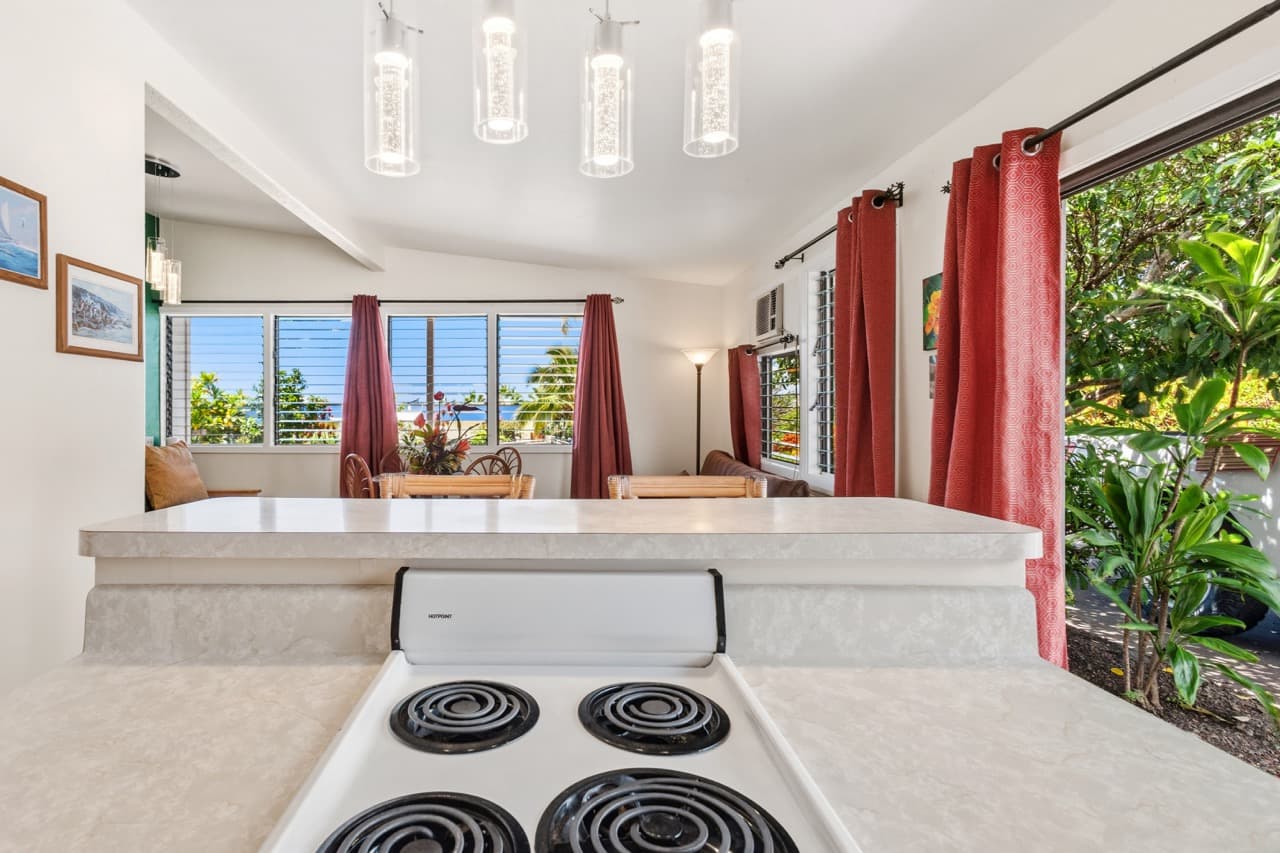 A modern kitchen view with a stove and dining area, featuring large windows and vibrant red curtains.