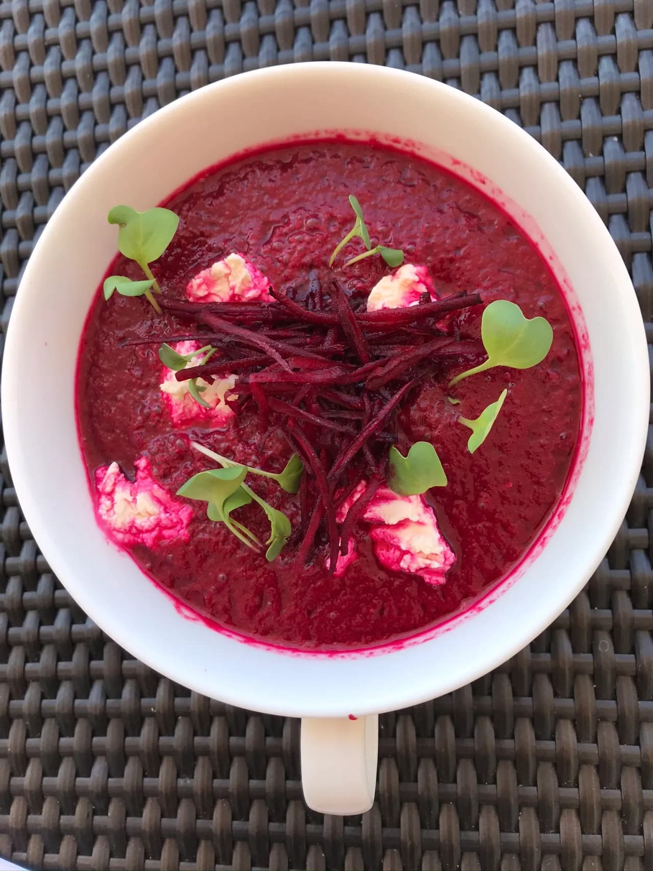A bowl of vibrant beet soup topped with sprigs of microgreens and dollops of creamy white garnish.