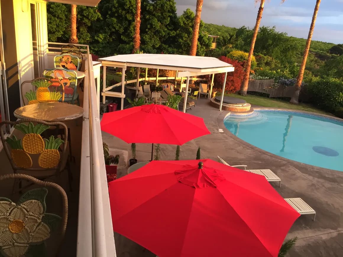 View of a pool area with red umbrellas and colorful chairs on a balcony.
