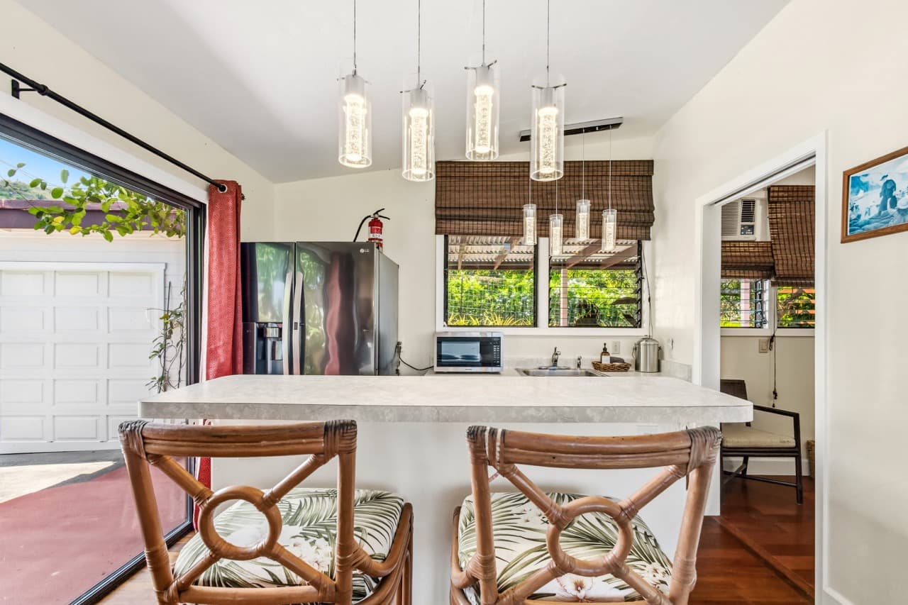 A bright kitchen with modern appliances and bar seating, featuring pendant lighting and large windows.