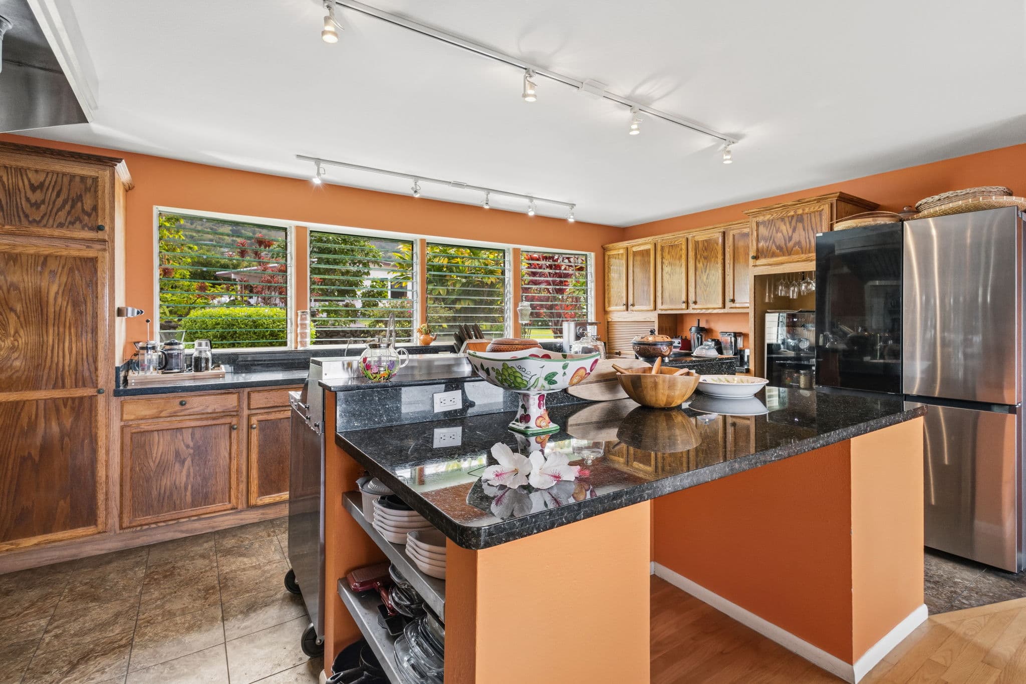 A modern kitchen featuring orange walls, a granite countertop island, and large windows with a view.