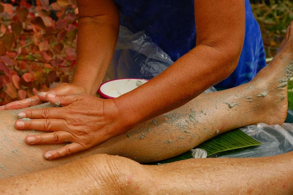 A person applies a mud treatment to a leg during a spa session.