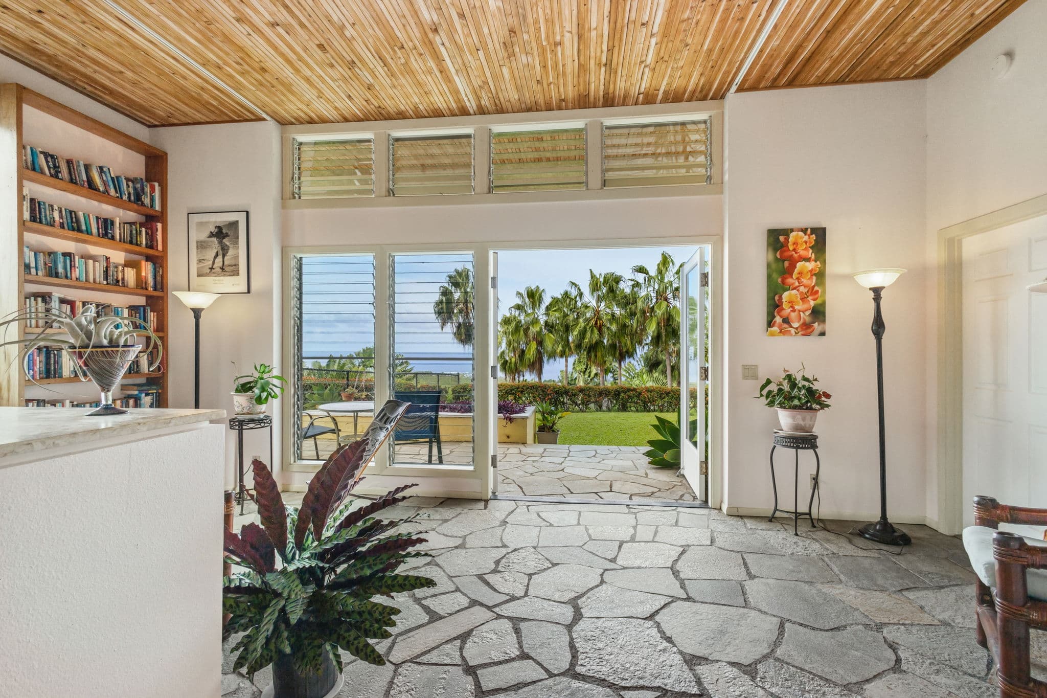 A bright entryway with a stone floor leads to an open patio surrounded by palm trees.