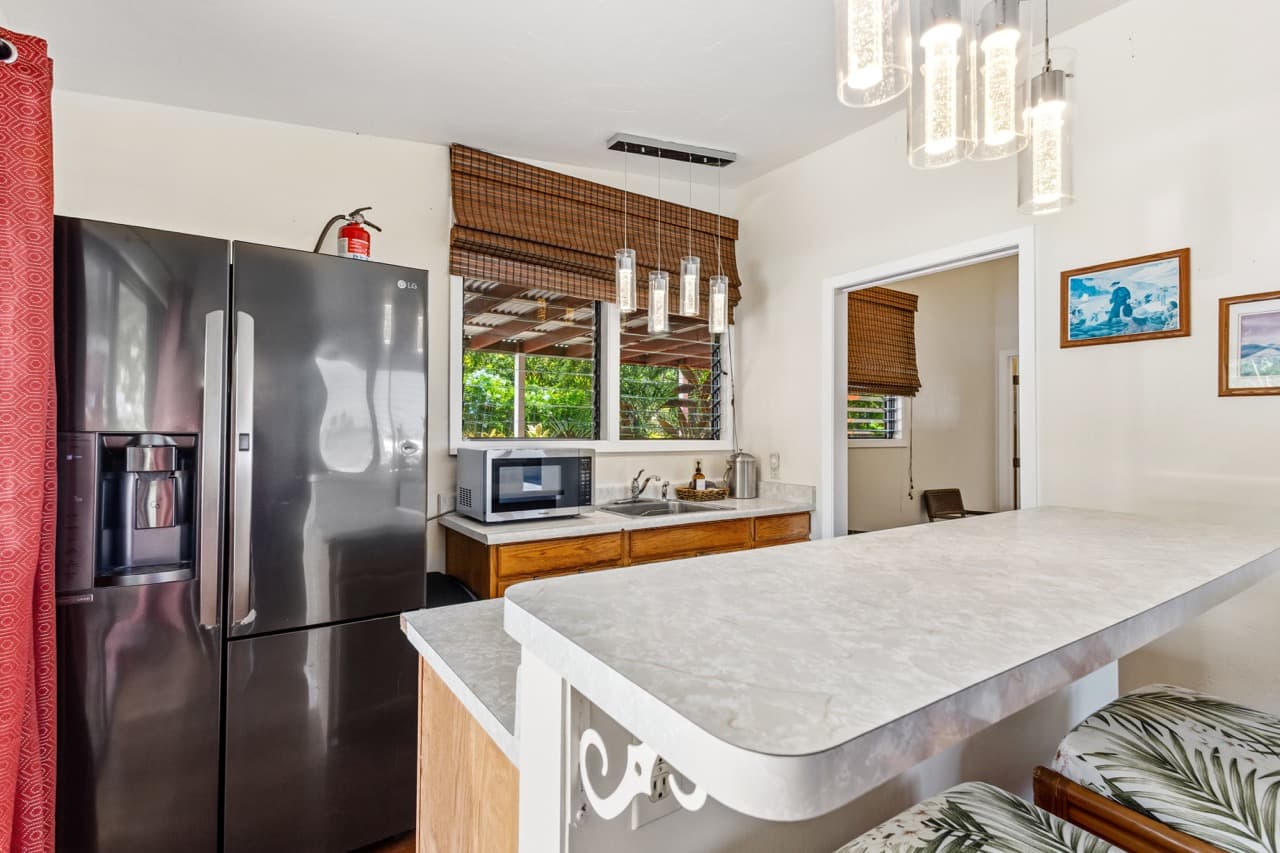 A modern kitchen featuring a fridge, microwave, and a bar countertop with tropical-patterned stools.