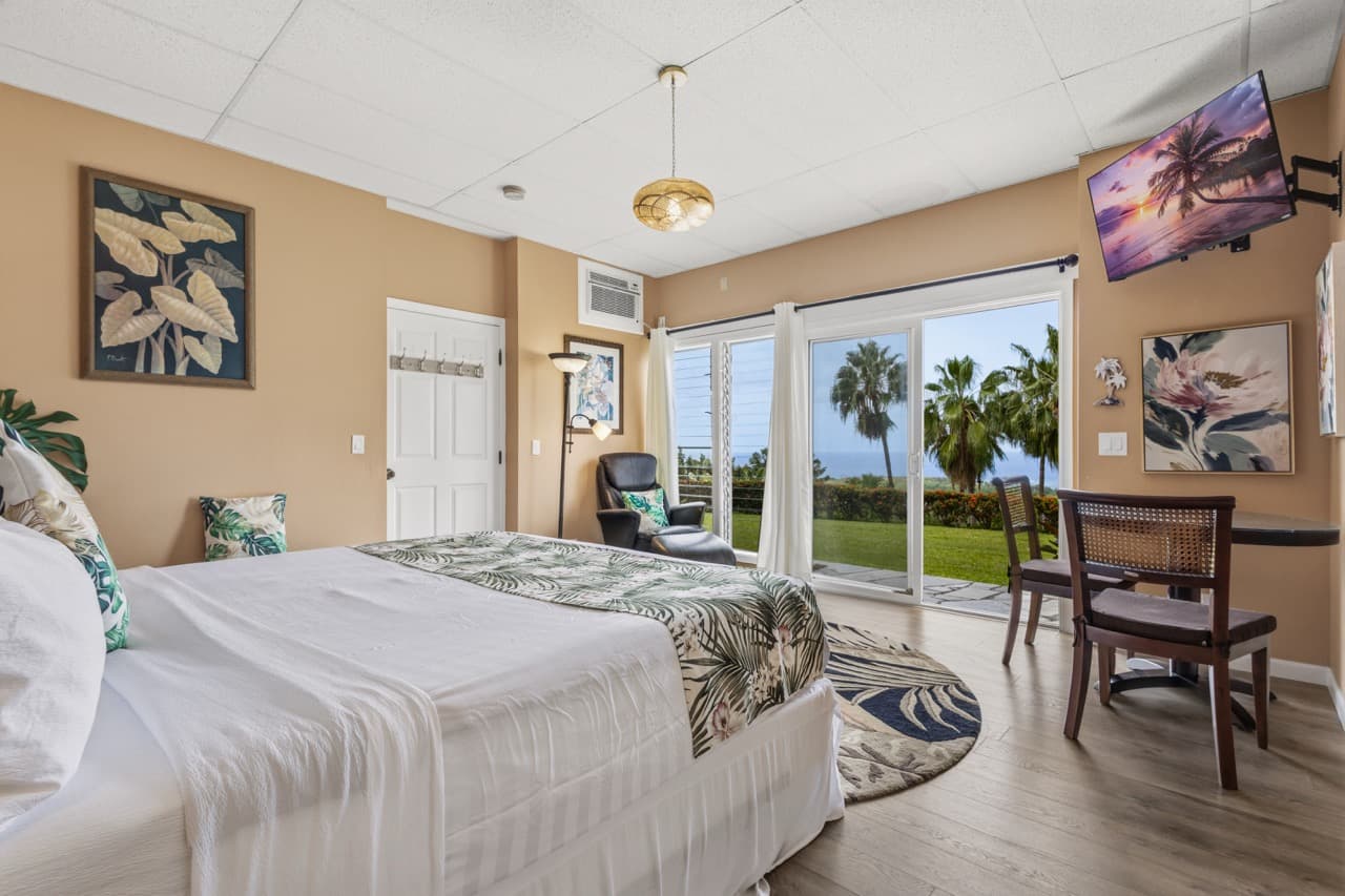 Cozy hotel room featuring a bed, seating area, and sliding glass door with garden and ocean view.