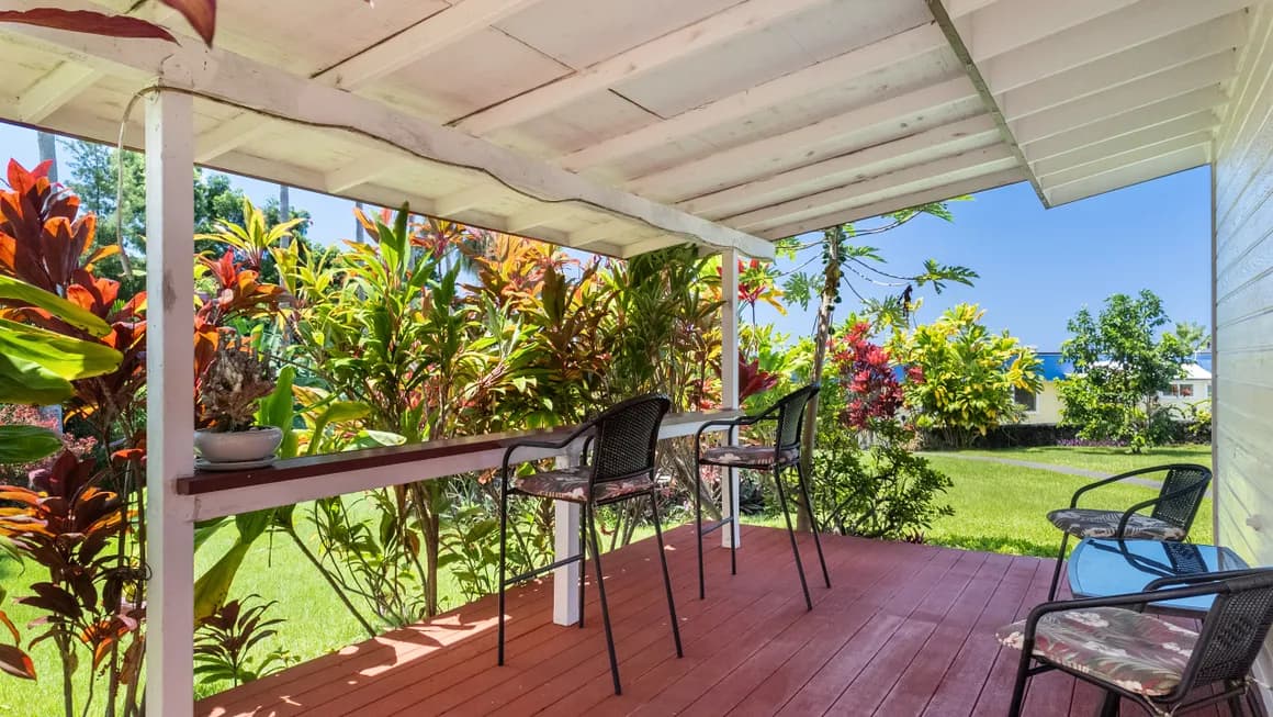 A covered patio with chairs overlooks a vibrant garden filled with tropical plants.