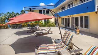 A sunny poolside area with lounge chairs, colorful umbrellas, and a modern building in the background.