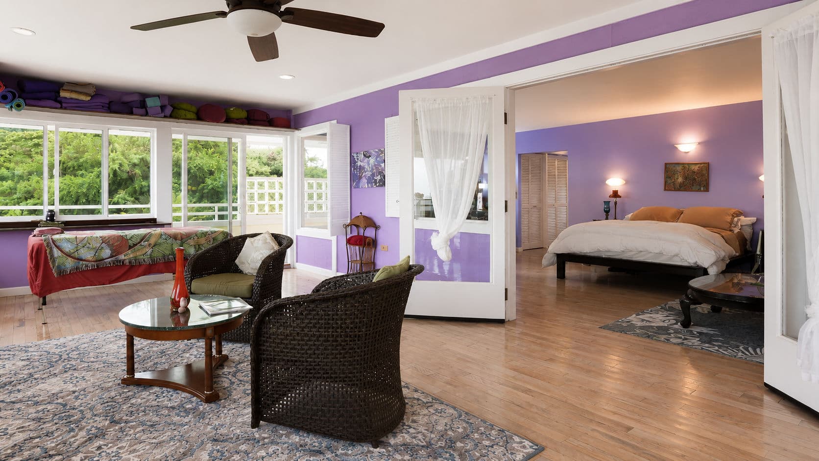 A brightly colored bedroom and sitting area with large windows and wooden flooring.
