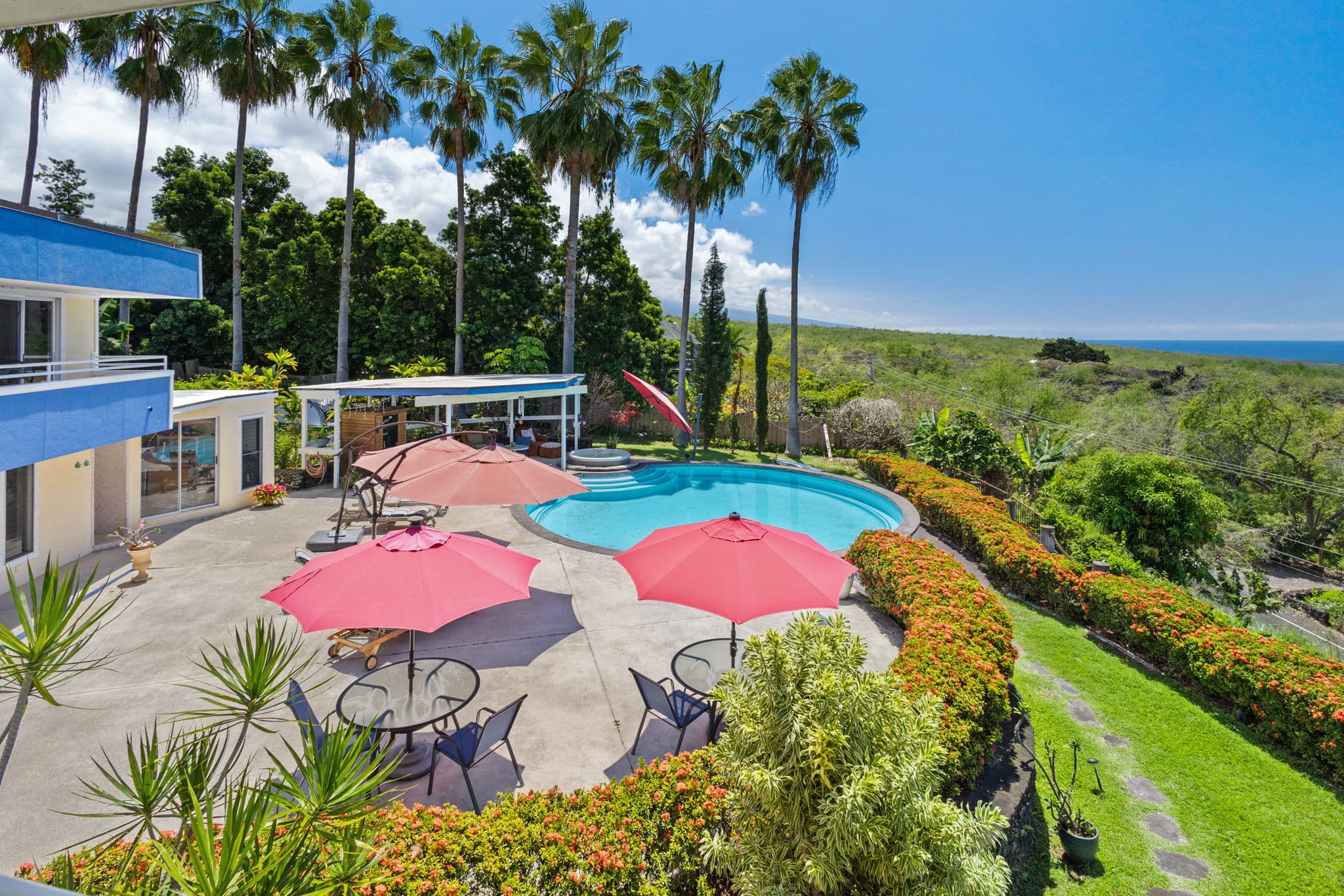 A luxurious outdoor pool area surrounded by tropical greenery and patio umbrellas.