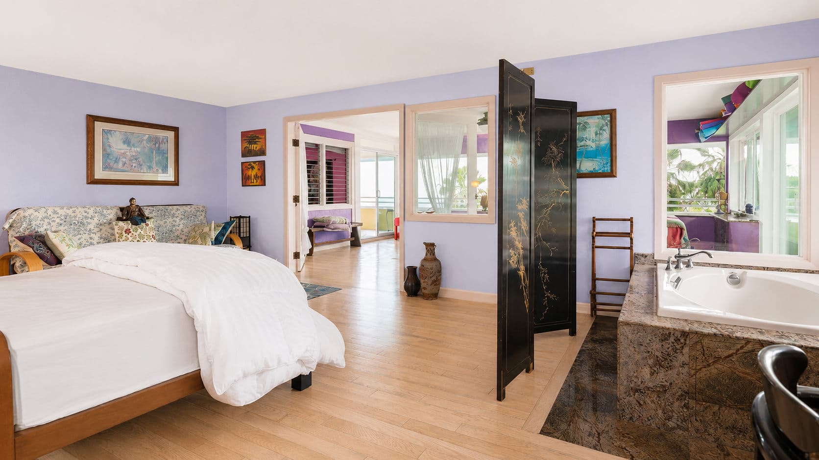 A bright, modern bedroom features a large bed, decorative screen, and views of a colorful adjoining room.