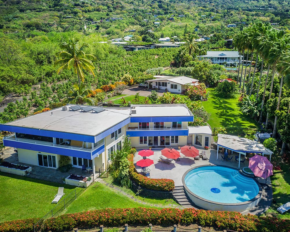 Aerial view of a modern villa with a pool surrounded by lush greenery and colorful landscaping.