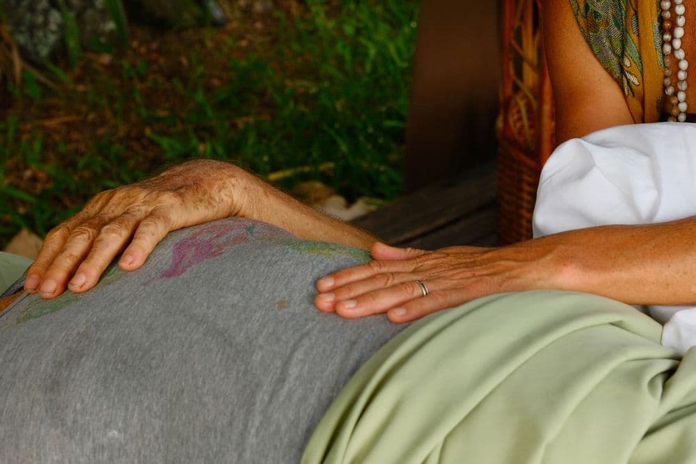 Two hands gently rest on a person's abdomen, surrounded by greenery.