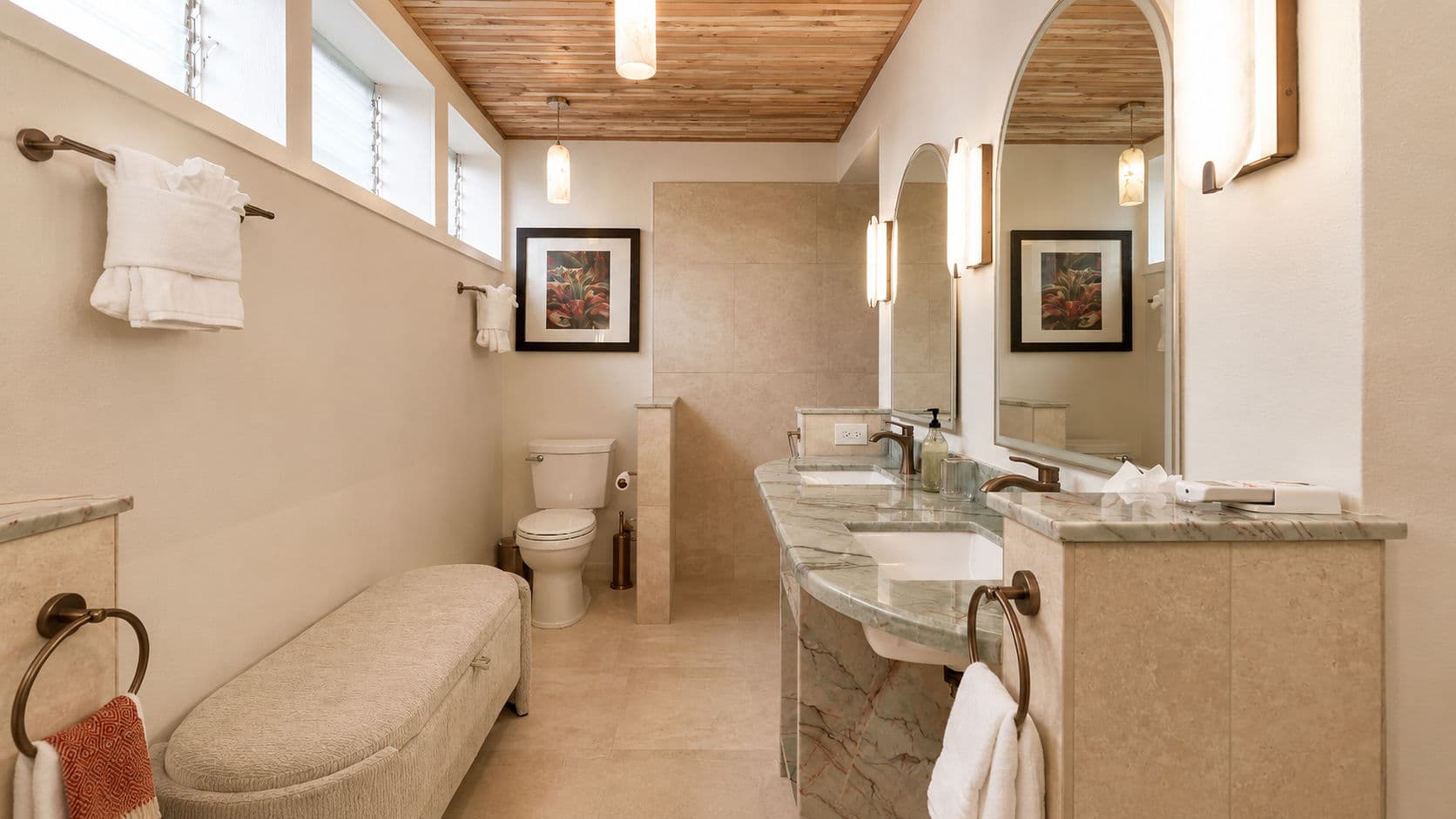 A modern bathroom featuring a double sink, storage bench, and decorative mirrors.