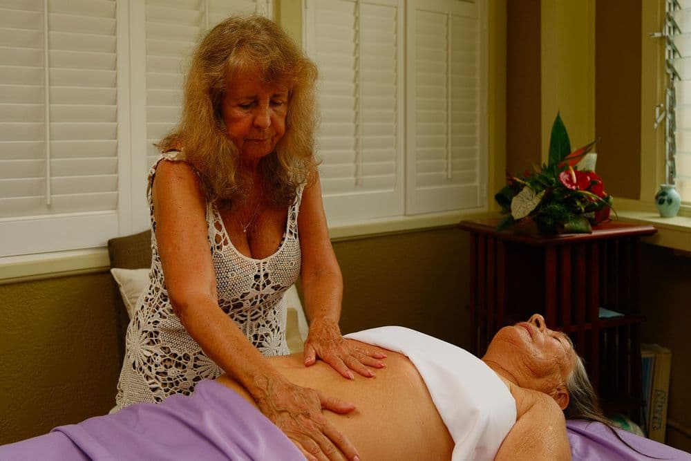 A massage therapist works on a client lying on a treatment table in a serene setting.