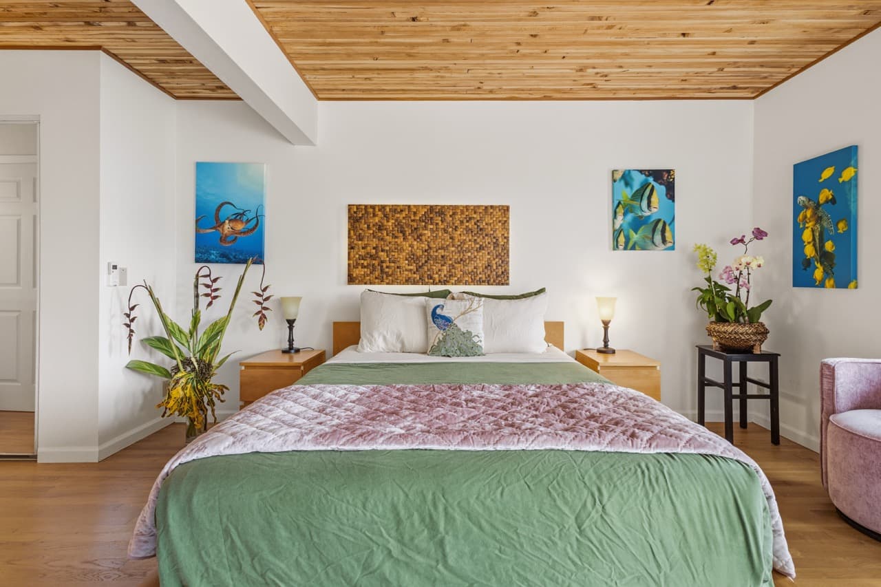 Bright, modern bedroom featuring a green bedspread, wooden ceiling, and vibrant artwork on the walls.