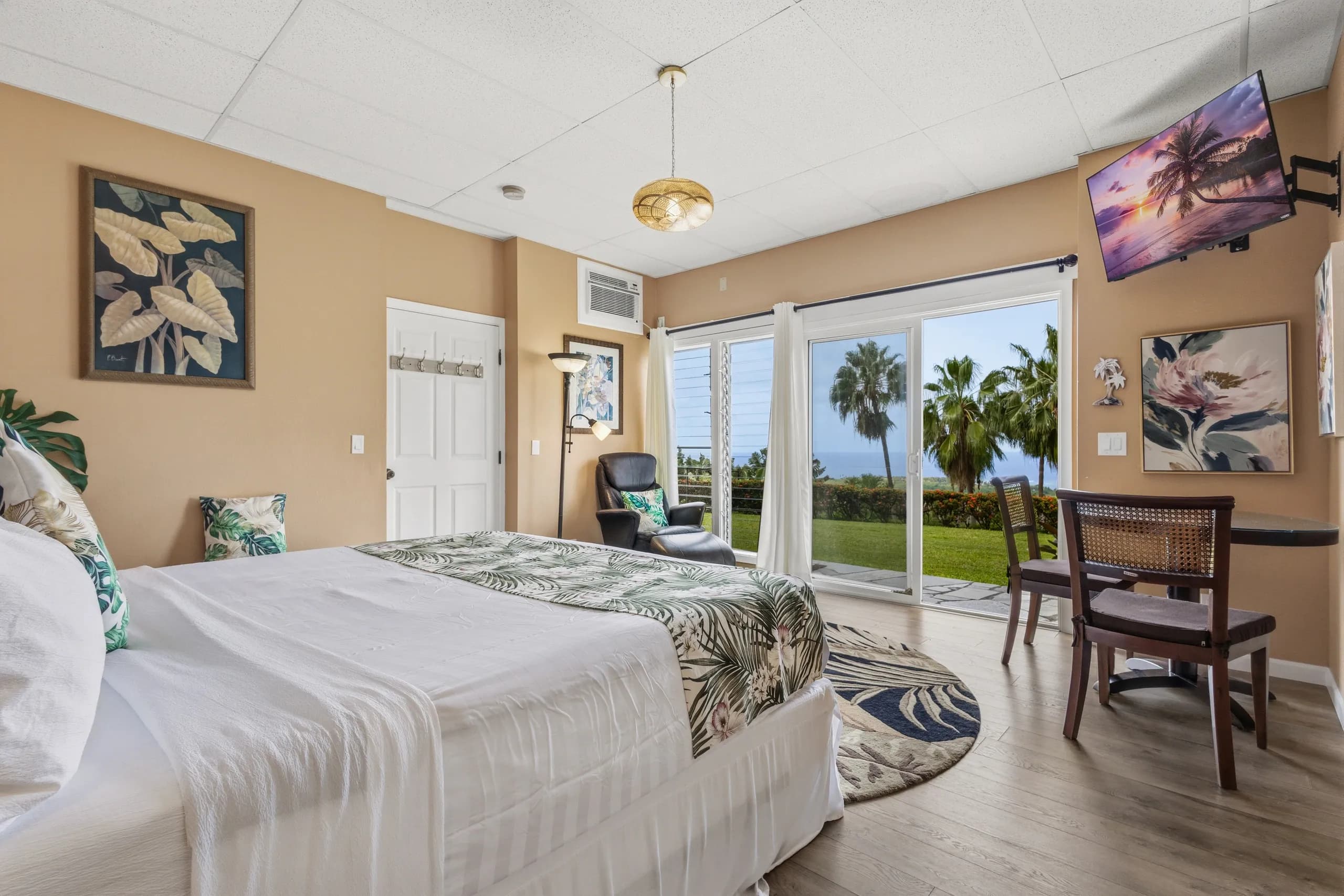 A cozy bedroom with a tropical theme and large windows showcasing a scenic view.