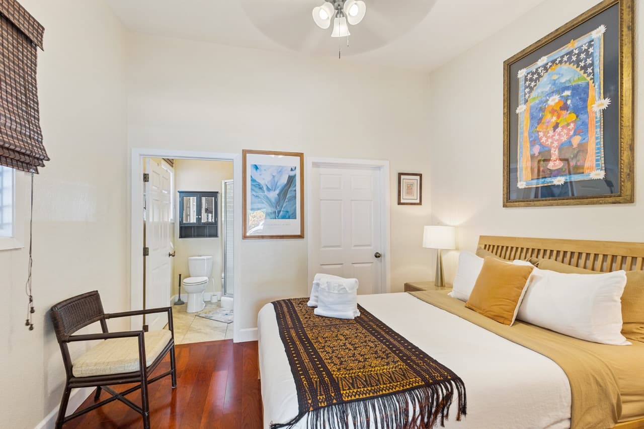 Cozy bedroom featuring a bed with decorative pillows, a chair, artwork on the walls, and a doorway leading to a bathroom.