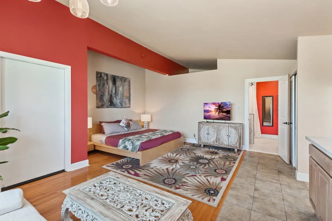 A modern bedroom featuring a bed with colorful linens, decorative rug, and an accent wall, with a doorway leading to a bathroom.