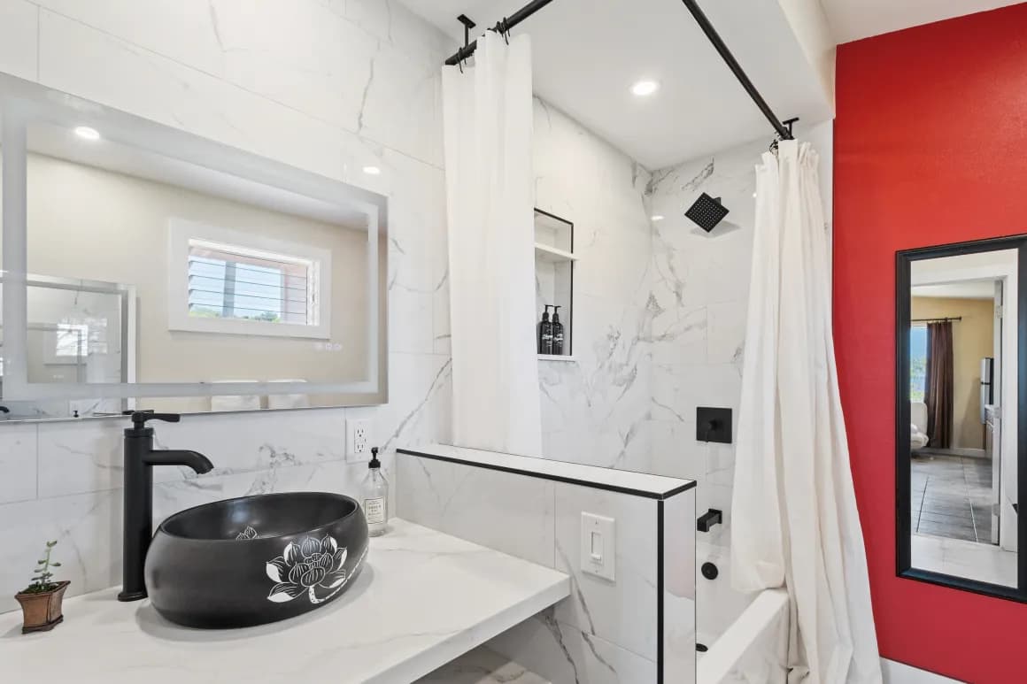 A modern bathroom featuring a sleek black sink, marble walls, a shower with a curtain, and a vibrant red accent wall.