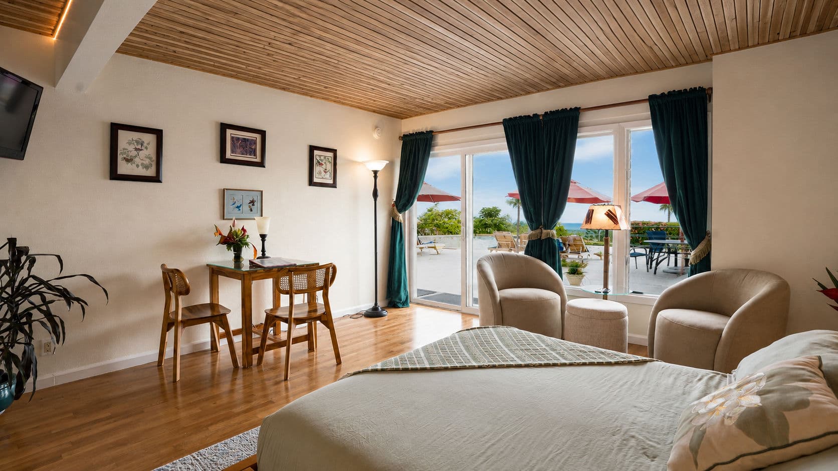 A cozy hotel room featuring a bed, a small dining table, and large windows overlooking a terrace with umbrellas.