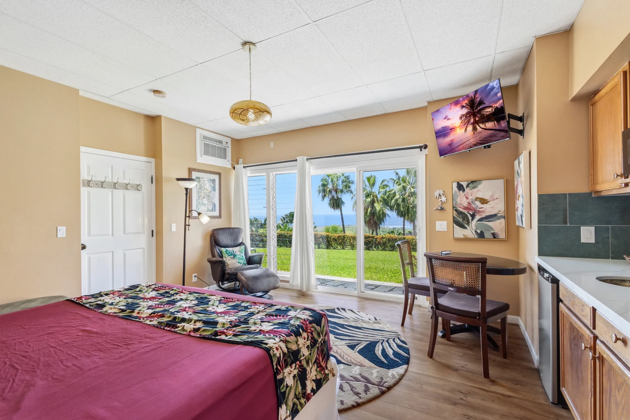 Cozy bedroom with a view of palm trees and the ocean through sliding glass doors.