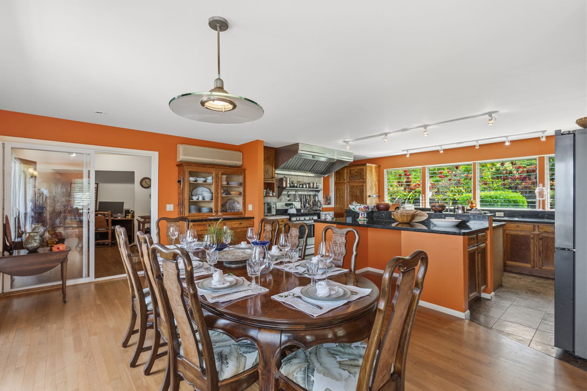 A bright kitchen and dining area featuring a wooden table set for dinner and large windows overlooking greenery.