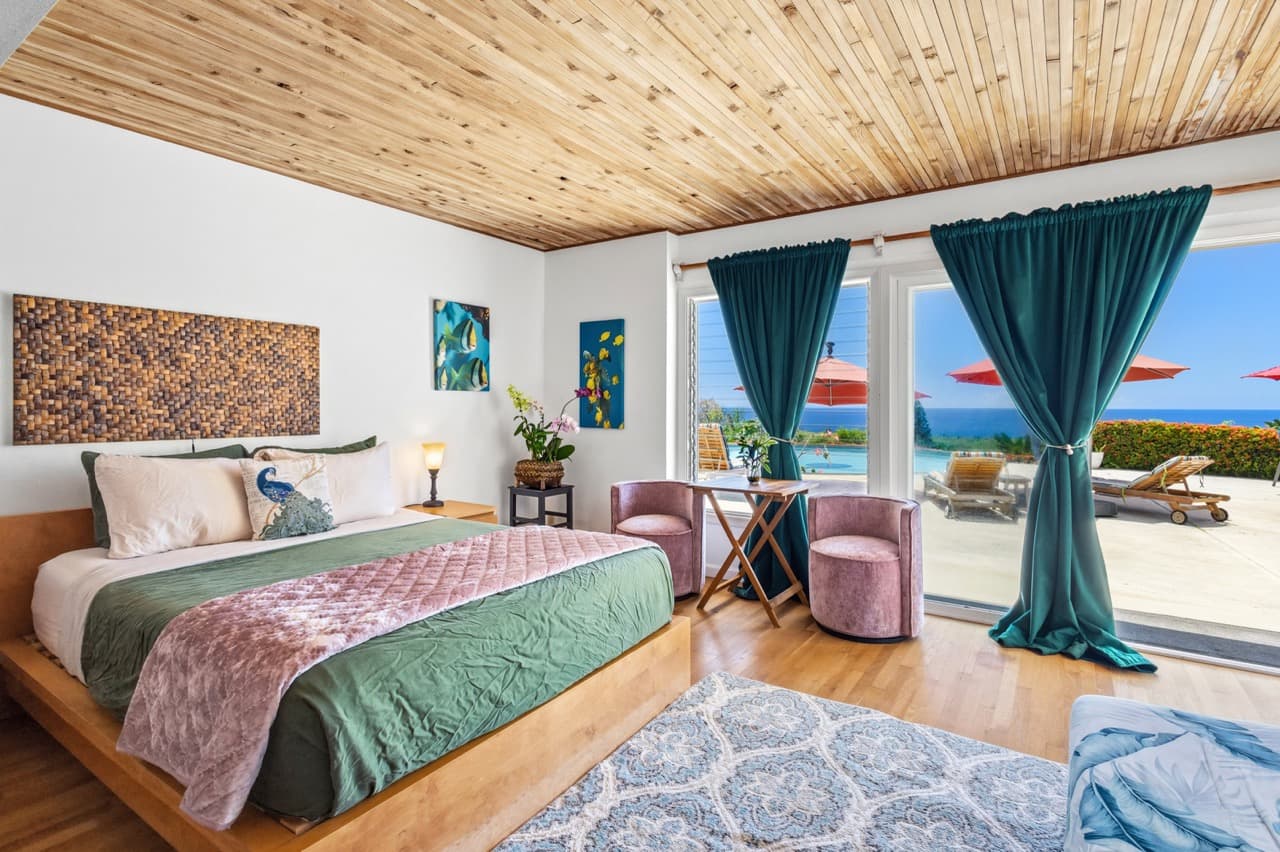 A stylish bedroom with a green bedspread, wooden ceiling, and large windows showcasing a view of the outdoors.