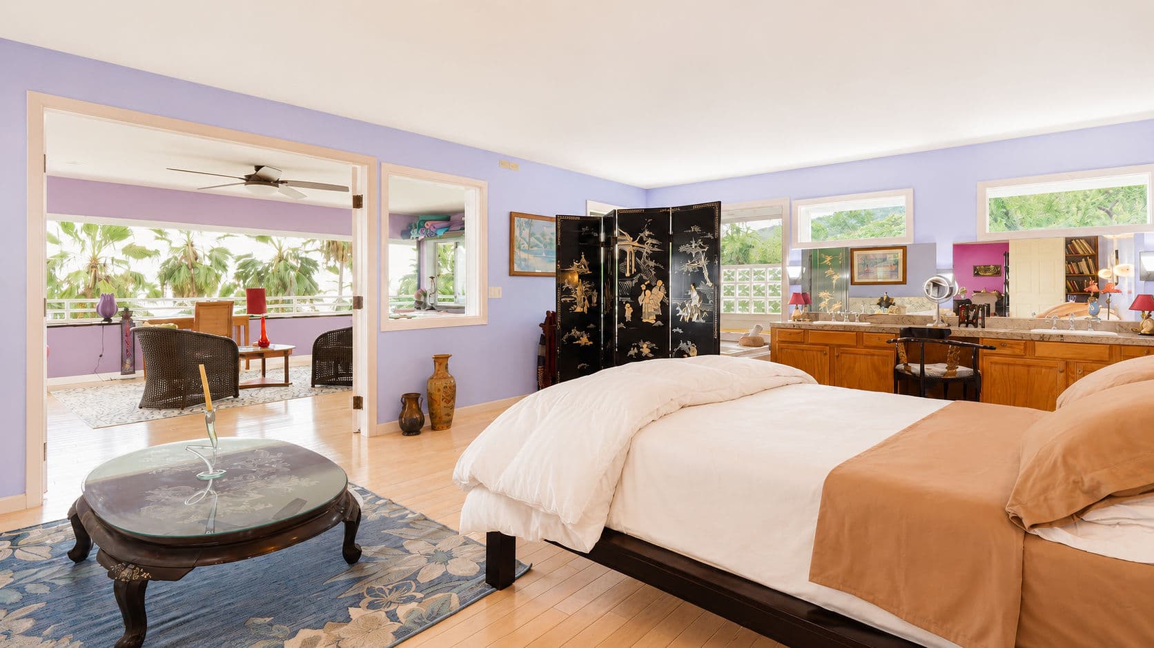 A bright and airy bedroom featuring a large bed, wooden furniture, and open views to a garden through multiple windows.