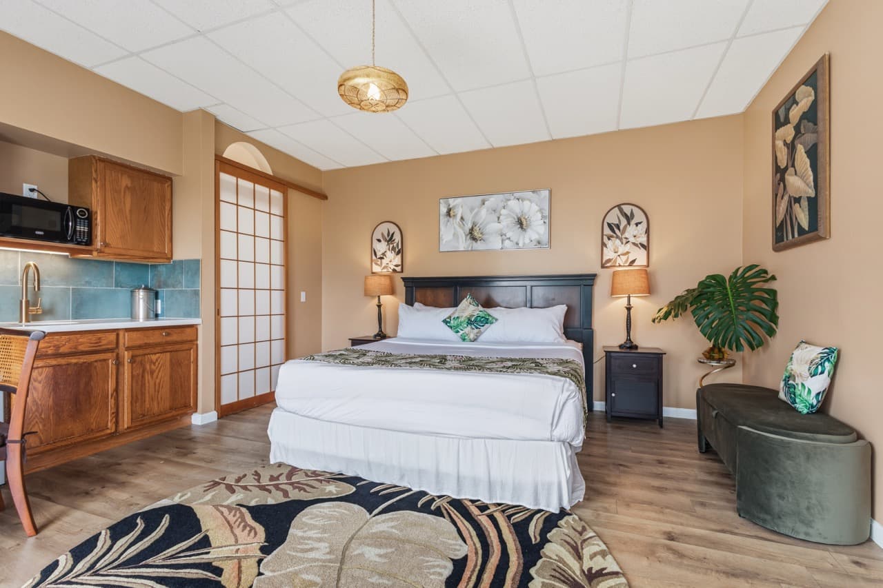 Cozy bedroom with a queen bed, kitchenette, and tropical decor.