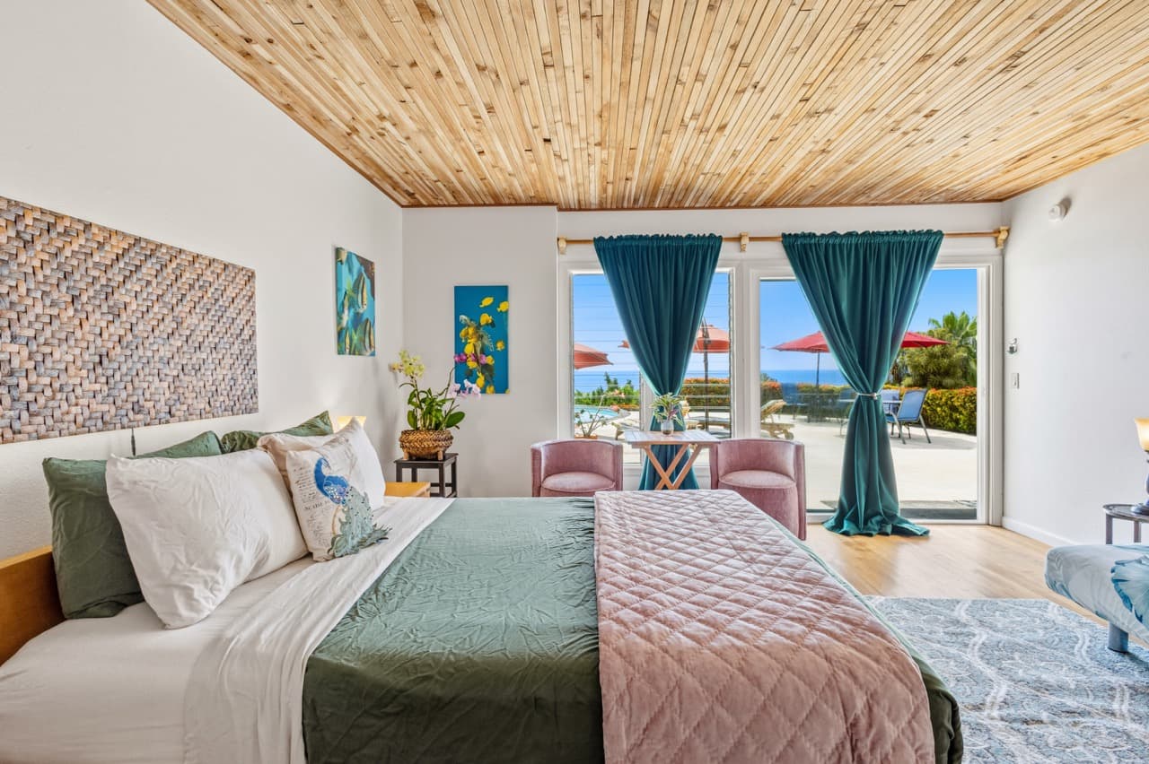 Bright and airy bedroom with a view of the outdoors, featuring a wooden ceiling, colorful decor, and inviting seating areas.