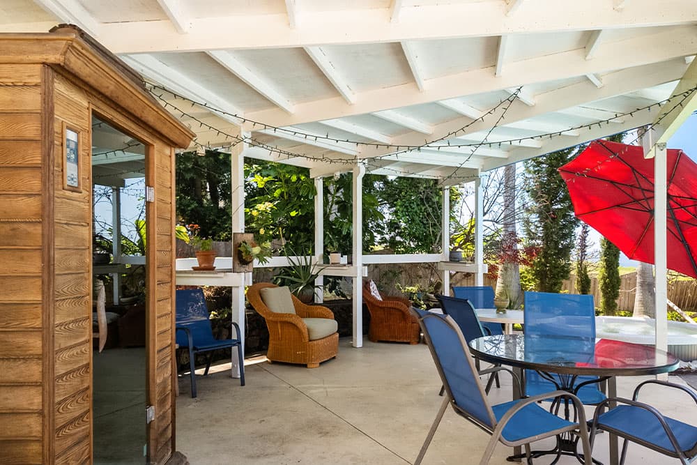 A shaded outdoor lounge area with comfortable seating, potted plants, and a red umbrella.