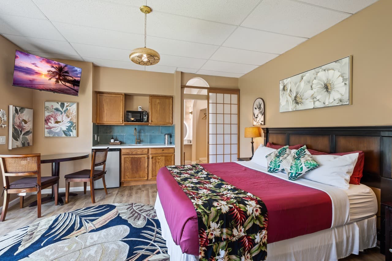A cozy bedroom featuring a king-size bed, kitchenette, and a television, all adorned with tropical decor.