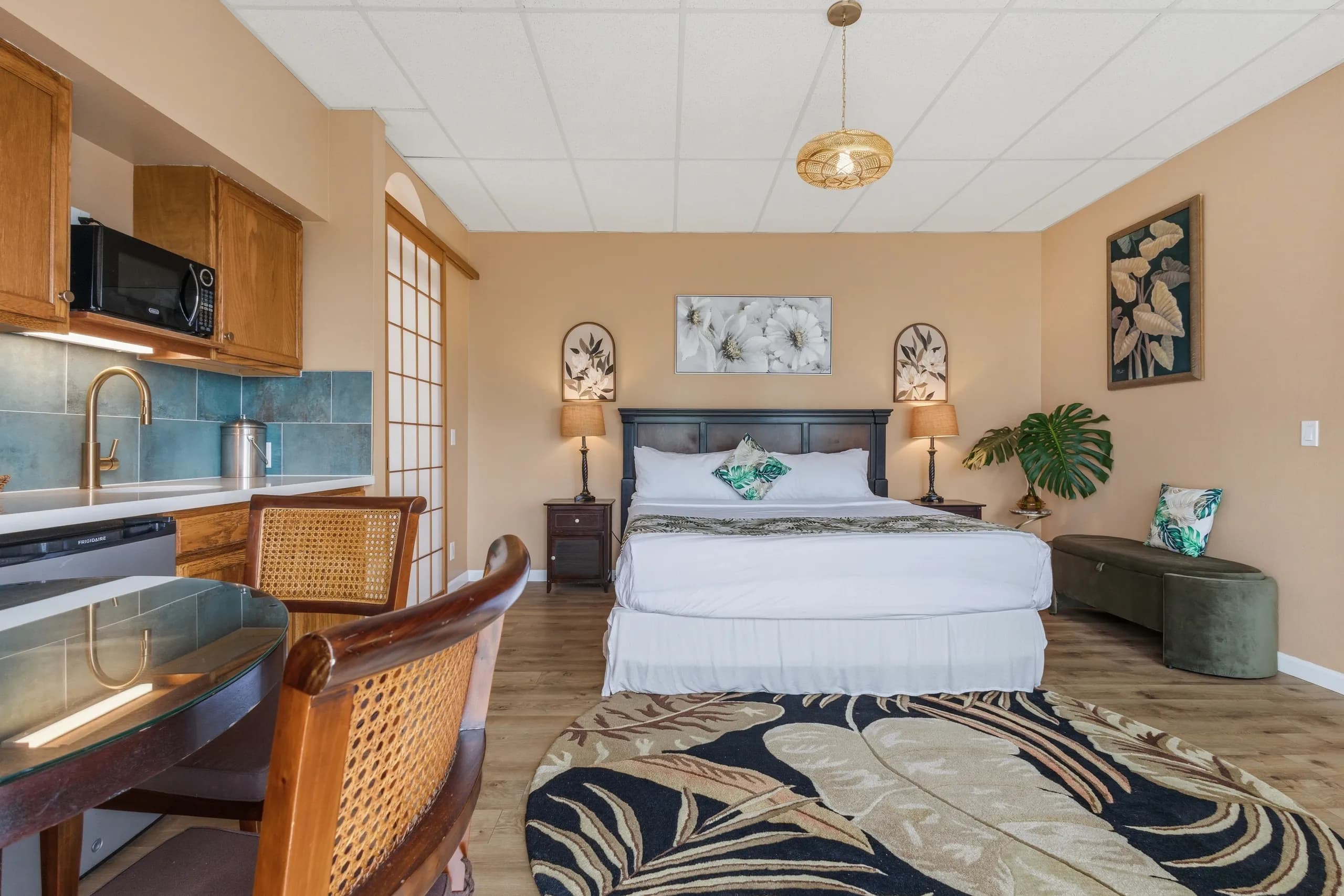 A well-decorated studio room with a bed, kitchenette, dining table, and tropical accents.