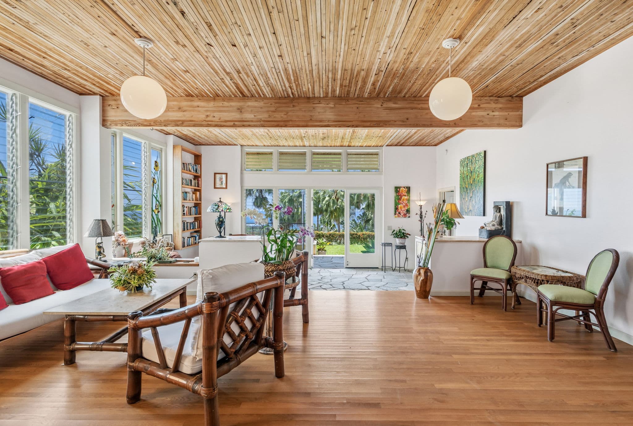 A bright living room with wooden ceilings, large windows, and tropical decor.